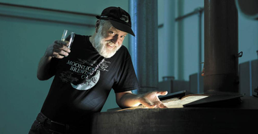 Moonlight Brewing founder Brian Hunt with glass of beer over a dimly lit beer tank