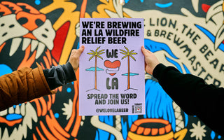 Closeup of two hands holding a We Love LA beer promotional poster against a vibrant mural