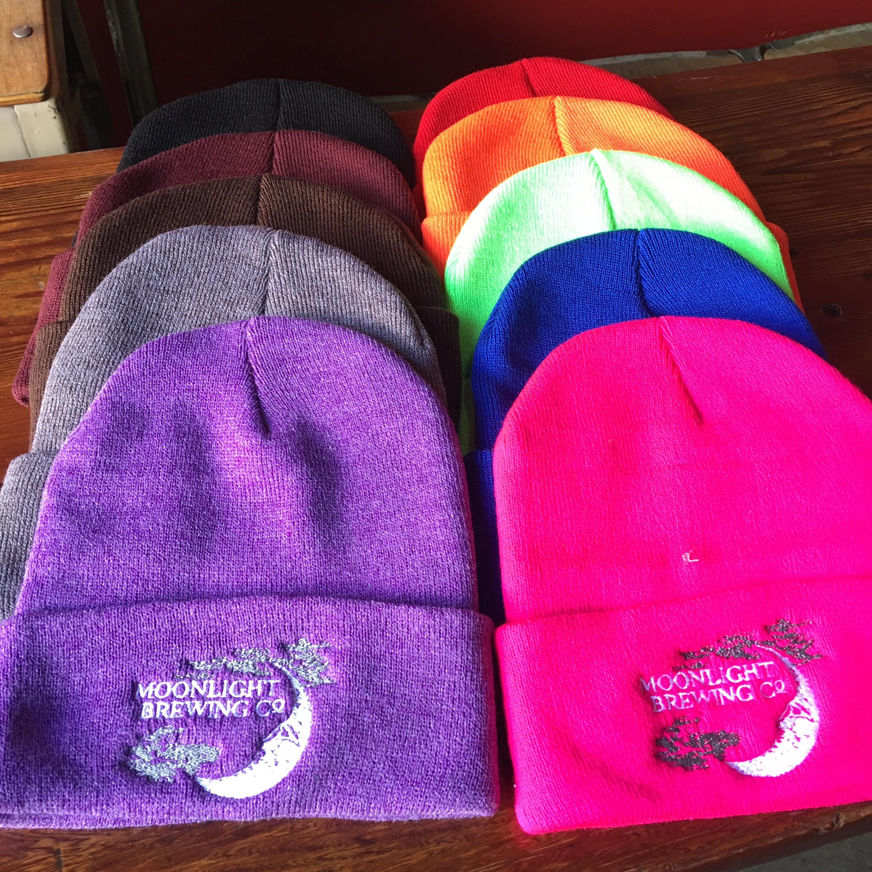 Collection of beanies in various colors with Moonlight Brewing logo on the front